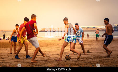 Gruppe von Jungen barfuß Teenager Jungs Fußball spielen an einem Sandstrand im Abendlicht mit dem Meer im Hintergrund Stockfoto