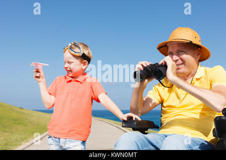 Behinderten Vater auf der Suche durch ein Fernglas mit Junge spielt mit Paper Plane Stockfoto