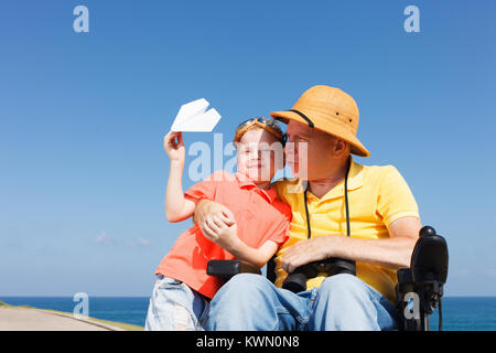 Behinderten Vater auf der Suche durch ein Fernglas mit Junge spielt mit Paper Plane Stockfoto