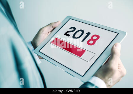Nahaufnahme eines jungen kaukasischen Mann in einem eleganten grauen Anzug hält eine digitale Tablet in der Hand mit der Nummer 2018, als das neue Jahr, laden in der scr Stockfoto