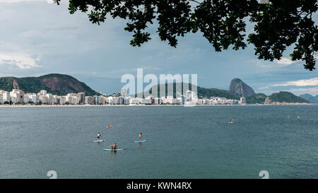 Up Paddle am Strand von Copacabana, Rio de Janeiro, Brasilien mit Gebäuden und Zuckerhut stehen Stockfoto