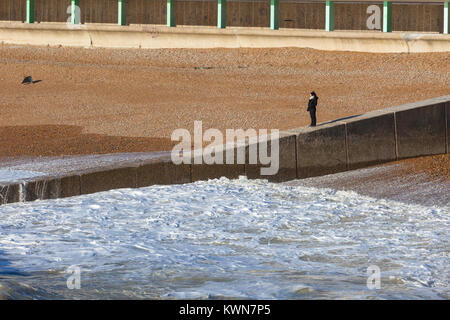 Eine einsame Frau schaut auf das Meer von der Hastings See Defense Wall, East Sussex, Großbritannien Stockfoto