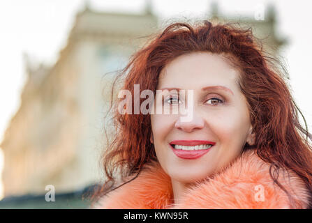 Nahaufnahme von einem schönen Lächeln reife Frau tragen orange Pelz Kragen mit alten Gebäude im Hintergrund Stockfoto