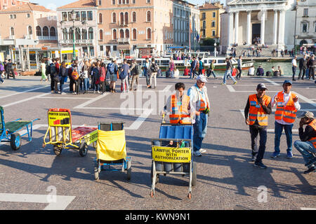 Hotel torhüter außerhalb von Santa Lucia Bahnhof, Cannaregio, Venice, Italien warten Touristen mit ihren Trolleys Gepäck zu transportieren Stockfoto