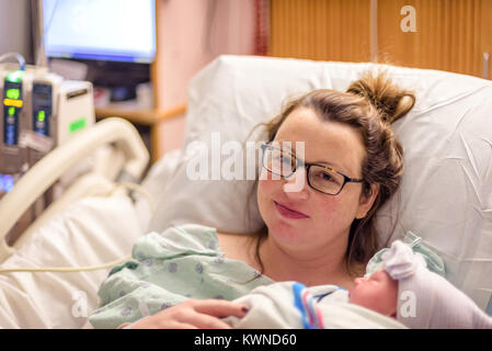 Glücklich und müde neue Mama holding Neugeborenes im Krankenhausbett nach Lieferung Stockfoto