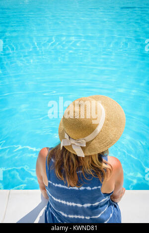 Ansicht der Frau in Stroh Sommer hat am Rand des Pool sitzend mit den Füßen im Wasser Stockfoto