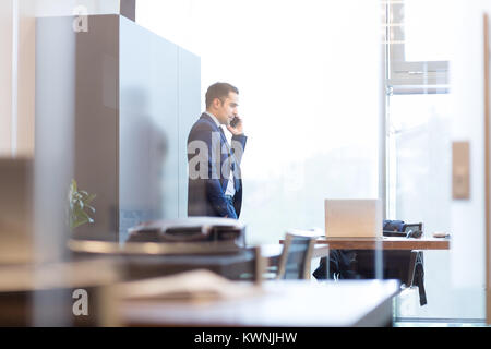 Geschäftsmann sprechen auf einem Handy beim Blick durch Fenster. Stockfoto