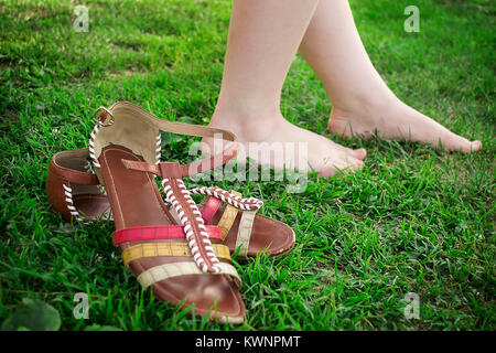 Sie zog ihr Sandalen und Spaziergänge barfuss im Gras. Stockfoto