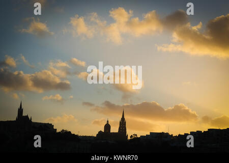 Mgarr, Gozo skyline Silhouette vom Meer mit Kirchen, Wolken und Sonnenuntergang Farben Stockfoto