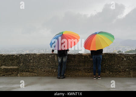 Zwei Menschen unter regenbogen farbe Schirme gegen den grauen Himmel Stockfoto