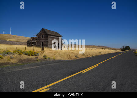 Abgebrochene Holzhaus in einer Wiese Feld hinter einem Zaun neben einer Hauptstraße mit gelben Linie Markierungen im Staat Washington, USA Stockfoto