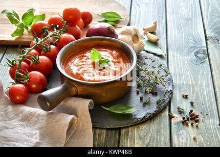 Tomaten Cremesuppe in einem dunklen Keramik Schüssel mit Sahne und Basilikum serviert. Zutaten: Tomaten, Paprika, Zwiebel und Knoblauch. Stockfoto