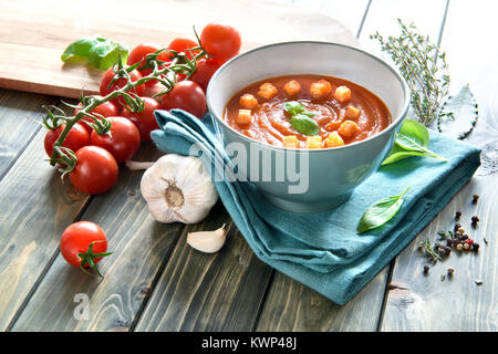 Tomaten Cremesuppe in einem türkis Keramik Schüssel auf eine passende Handtuch serviert mit Croutons und Basilikum. Zutaten: Tomaten, Paprika, Zwiebel und Knoblauch. Stockfoto