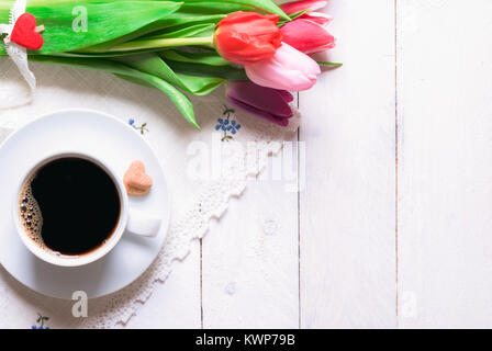 Schönen Blumenstrauß aus Tulpen gebunden mit Spitze und einer Tasse Kaffee und herzförmige Zucker, auf einem vintage Küche Handtuch, auf einem weißen Holztisch. Stockfoto