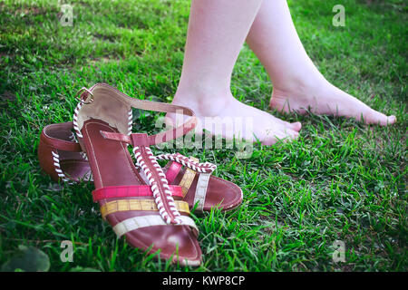 Sie zog ihr Sandalen und Spaziergänge barfuss im Gras Stockfoto