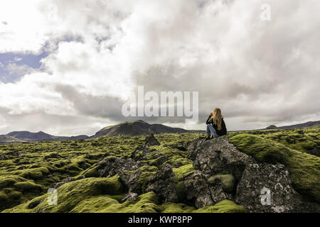 Junge Frau sitzt auf Felsen und Suchen an der majestätischen isländische Landschaft Stockfoto