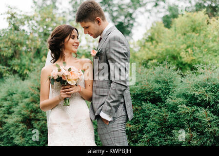 Hübscher Bräutigam im grauen Anzug lehnt sich zu winzigen Braut Stockfoto
