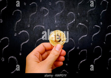 Frau hand mit goldenen Bitcoin virtuelles Geld gegen Tafel mit Fragezeichen. Stockfoto