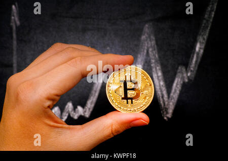 Tambow, Russische Föderation - Dezember 27, 2017, Frau mit goldenen Bitcoin virtuelles Geld gegen Tafel mit Kreide Zeichnen von Graphen. Stockfoto