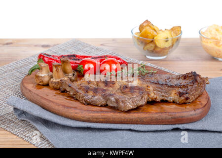 Detaillierte Ansicht von lecker lecker Gegrilltes Steak auf Holzplatte mit Kartoffel, Tomate und roter Pfeffer serviert. Stockfoto