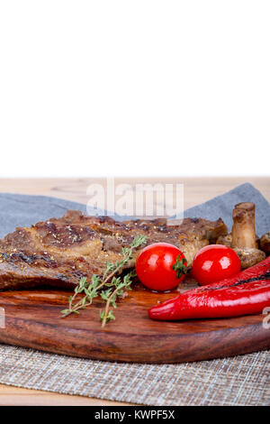 Detaillierte Ansicht von lecker lecker Gegrilltes Steak auf Holzplatte mit Kartoffel, Tomate und roter Pfeffer serviert. Stockfoto