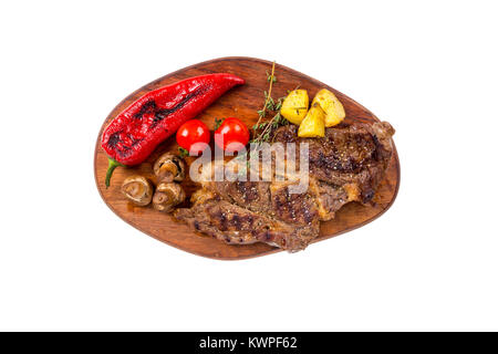 Detaillierte Ansicht von lecker lecker Gegrilltes Steak auf Holzplatte mit Kartoffel, Tomate und Paprika diente, auf weißem Hintergrund. Stockfoto