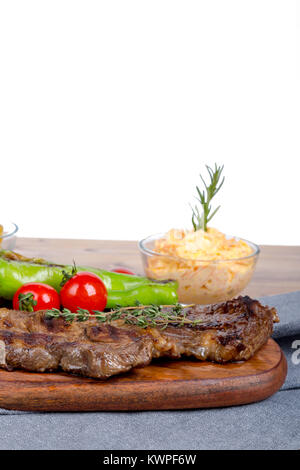 Detaillierte Ansicht von lecker lecker Gegrilltes Steak auf Holzplatte mit Kartoffel, Tomate und roter Pfeffer serviert. Stockfoto
