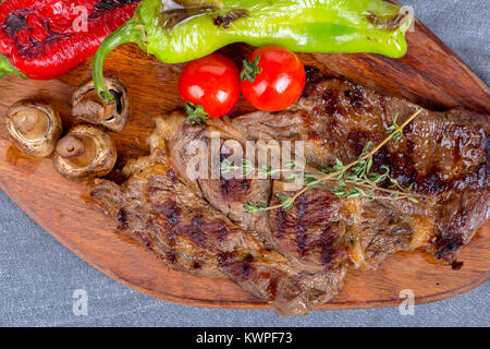 Detaillierte Ansicht von lecker lecker Gegrilltes Steak auf Holzplatte mit Kartoffel, Tomate und roter Pfeffer serviert. Stockfoto