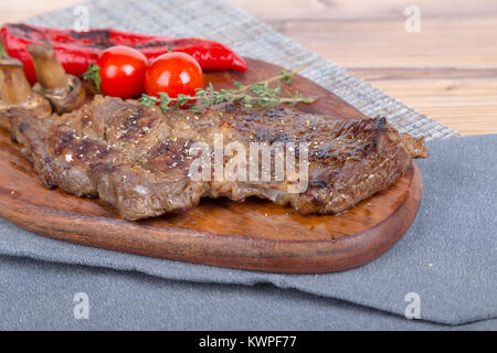 Detaillierte Ansicht von lecker lecker Gegrilltes Steak auf Holzplatte mit Kartoffel, Tomate und roter Pfeffer serviert. Stockfoto