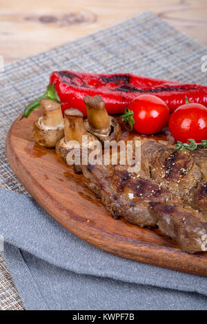 Detaillierte Ansicht von lecker lecker Gegrilltes Steak auf Holzplatte mit Kartoffel, Tomate und roter Pfeffer serviert. Stockfoto