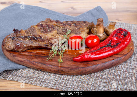 Detaillierte Ansicht von lecker lecker Gegrilltes Steak auf Holzplatte mit Kartoffel, Tomate und roter Pfeffer serviert. Stockfoto