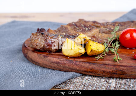 Detaillierte Ansicht von lecker lecker Gegrilltes Steak auf Holzplatte mit Kartoffel, Tomate und roter Pfeffer serviert. Stockfoto
