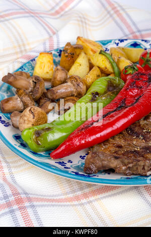 Detaillierte Ansicht von lecker lecker Gegrilltes Steak auf Holzplatte mit Kartoffel, Tomate und roter Pfeffer serviert. Stockfoto