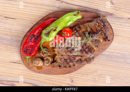 Detaillierte Ansicht von lecker lecker Gegrilltes Steak auf Holzplatte mit Kartoffel, Tomate und roter Pfeffer serviert. Stockfoto