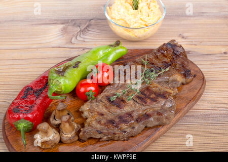 Detaillierte Ansicht von lecker lecker Gegrilltes Steak auf Holzplatte mit Kartoffel, Tomate und roter Pfeffer serviert. Stockfoto