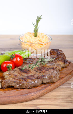 Detaillierte Ansicht von lecker lecker Gegrilltes Steak auf Holzplatte mit Kartoffel, Tomate und roter Pfeffer serviert. Stockfoto