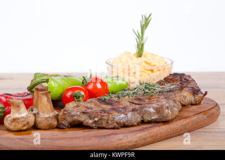 Detaillierte Ansicht von lecker lecker Gegrilltes Steak auf Holzplatte mit Kartoffel, Tomate und roter Pfeffer serviert. Stockfoto