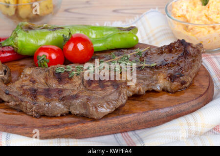 Detaillierte Ansicht von lecker lecker Gegrilltes Steak auf Holzplatte mit Kartoffel, Tomate und roter Pfeffer serviert. Stockfoto