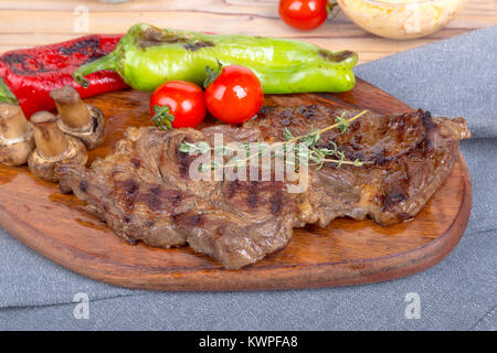 Detaillierte Ansicht von lecker lecker Gegrilltes Steak auf Holzplatte mit Kartoffel, Tomate und roter Pfeffer serviert. Stockfoto