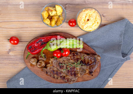 Detaillierte Ansicht von lecker lecker Gegrilltes Steak auf Holzplatte mit Kartoffel, Tomate und roter Pfeffer serviert. Stockfoto