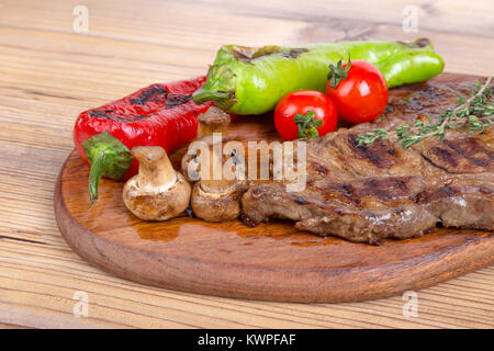 Detaillierte Ansicht von lecker lecker Gegrilltes Steak auf Holzplatte mit Kartoffel, Tomate und roter Pfeffer serviert. Stockfoto
