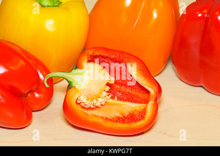 Organische Rot, Gelb und Orange Paprika auf Ahornholz, Nahaufnahme, mit einem Pfeffer in zwei Hälften geschnitten. Stockfoto