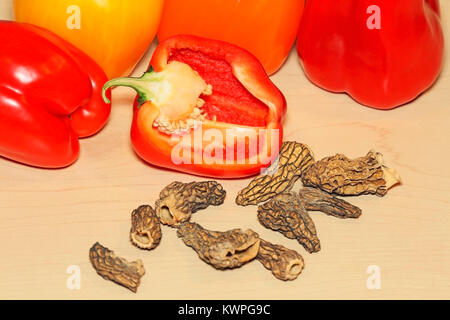 Organische Rot, Gelb und Orange Paprika und getrocknete Morcheln auf Ahornholz, Nahaufnahme, mit einem Pfeffer in zwei Hälften geschnitten. Stockfoto