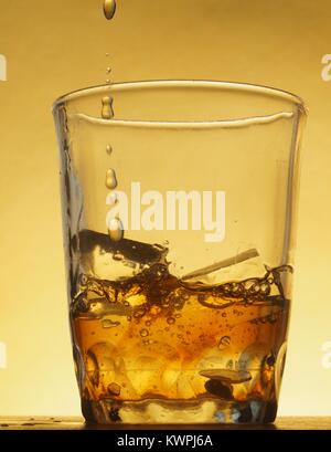 Transparentes Glas tumbler mit Eiswürfeln. In ein Glas mit Getränken gefüllt. Ein Trickle der Flüssigkeit. Foto auf einem gelben Hintergrund. Immer noch leben. Stockfoto