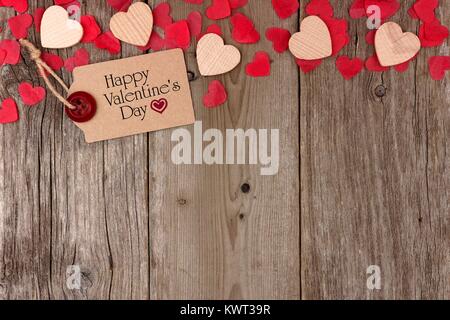 Happy Valentines Tag Geschenk tag mit verstreuten Holz- Herzen und Konfetti oberer Rand auf einer rustikalen, mit Holz Hintergrund Stockfoto