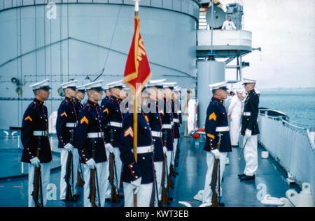 Eine Gruppe von United States Marine Corps (USMC) Mitglieder in Uniform stehen stramm und eine Flagge auf einem Schiff, mit der United States Navy Segler im Hintergrund, 1958. () Stockfoto