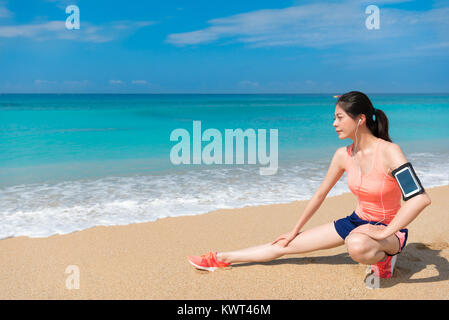 Lächelnd hübsche Läuferin, Ausfallschritt posing zum Aufwärmen, wenn Sie zum Strand fahren und das Tragen von Sportswear Vorbereitung Training. Stockfoto