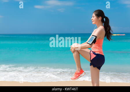 Seitenansicht Foto der Schönen lächelnde Frau Athlet Warm-up am Strand und Stretching Bein, wenn sie der Vorbereitung Lauftraining. Stockfoto