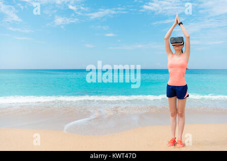 Attraktive junge Sportlerin, die Schwimmer vorbereiten Haltung stehend auf Strand, wenn Sie tragen Virtuelle Realität Schutzbrille zu beobachten, 3D-Video. Stockfoto