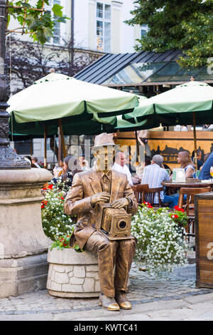 Lemberg, Ukraine - Juli 22, 2017: lebende Statue gold Fotograf mit der Kamera sitzt auf Beet mit Blumen, Sommertag an Stadt Stockfoto